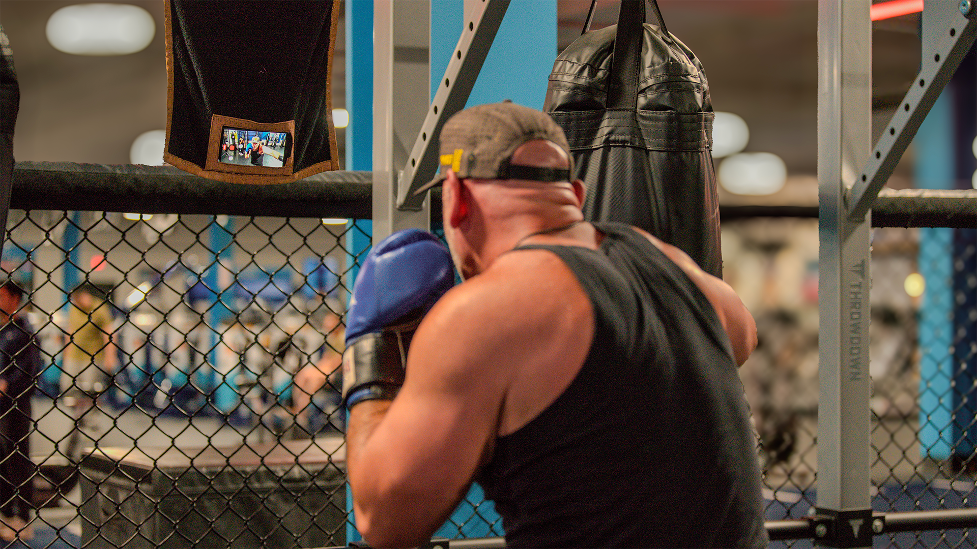 Man boxing practice while recording training content using media towel at gym.