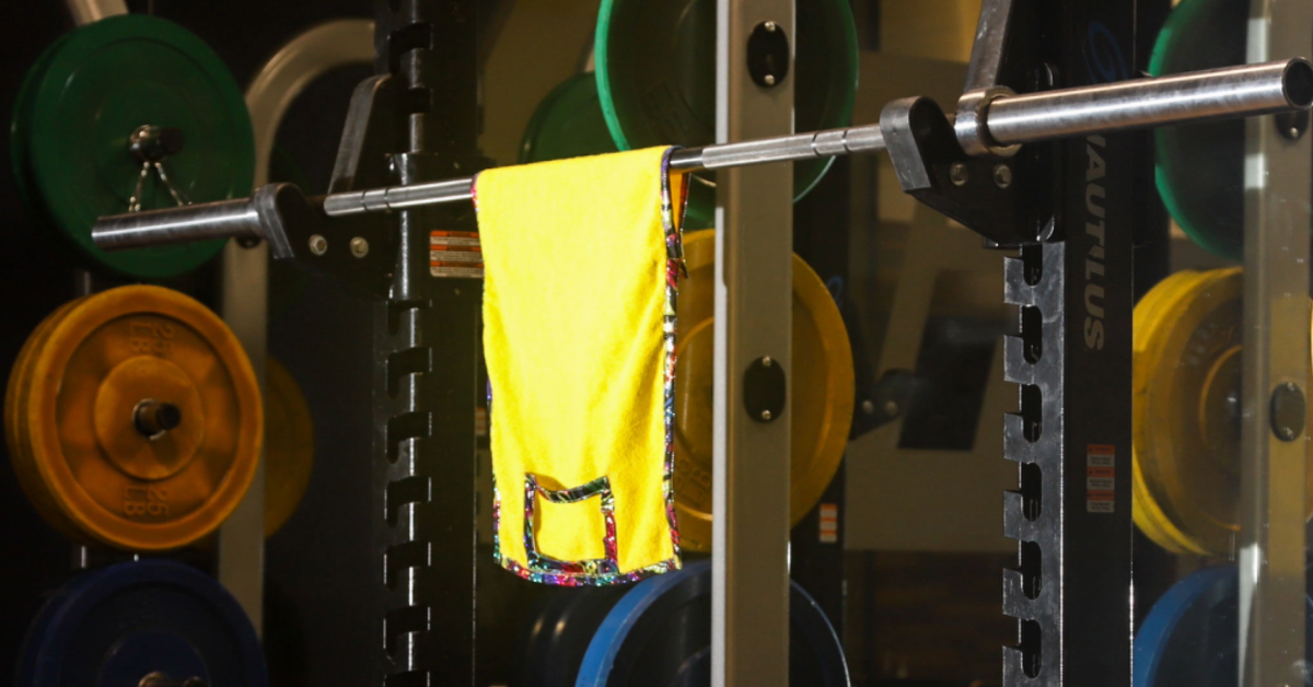 Yellow Zumba Media Towel wrapped around squat bar hanging in gym.