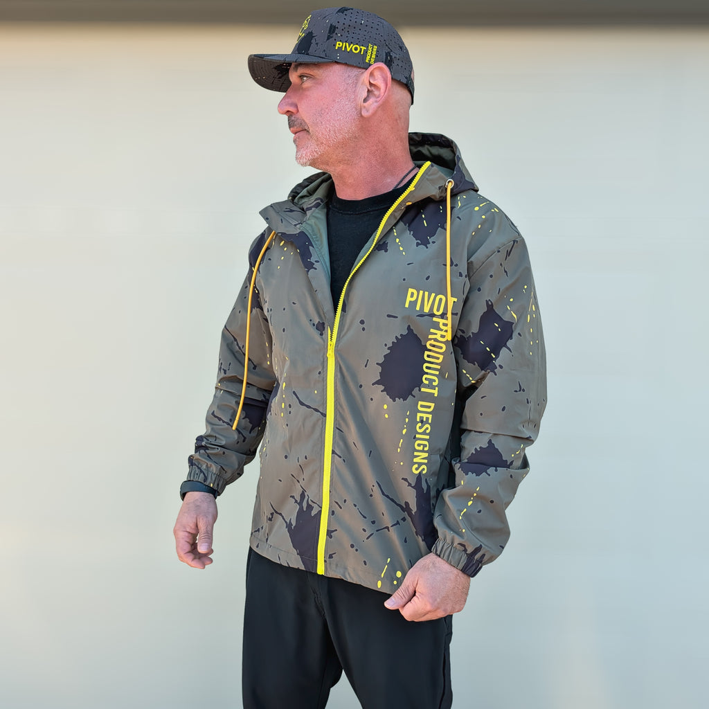 Man wearing a camouflage jacket with yellow accents and a cap, standing outside.