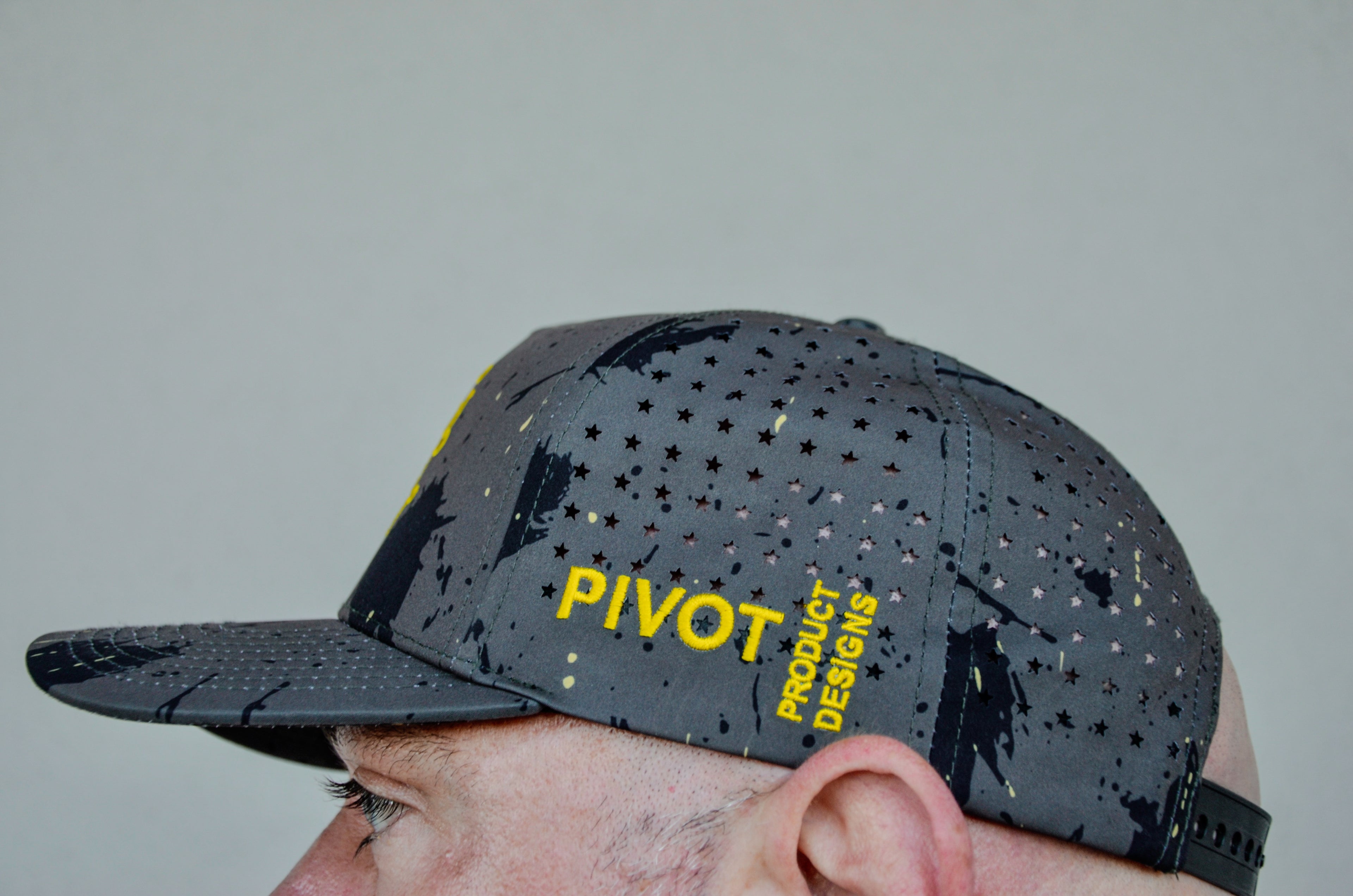 Man wearing a camo hat with American stars vent holes and yellow 'PIVOT' branding.