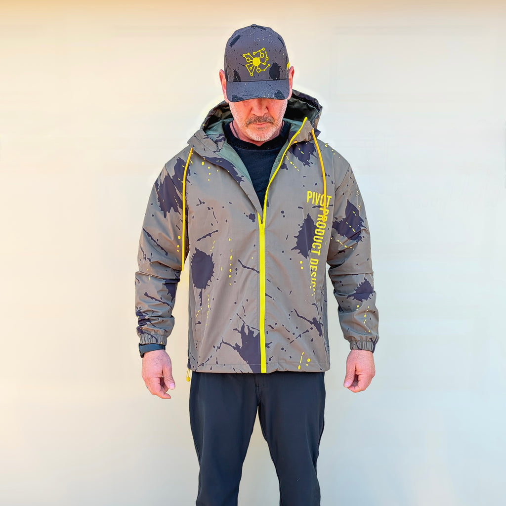 Man wearing a detailed camouflage jacket with yellow accents and a matching cap against a plain background