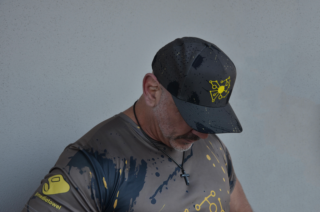 Man wearing a dark camo cap with a yellow logo and a matching shirt.