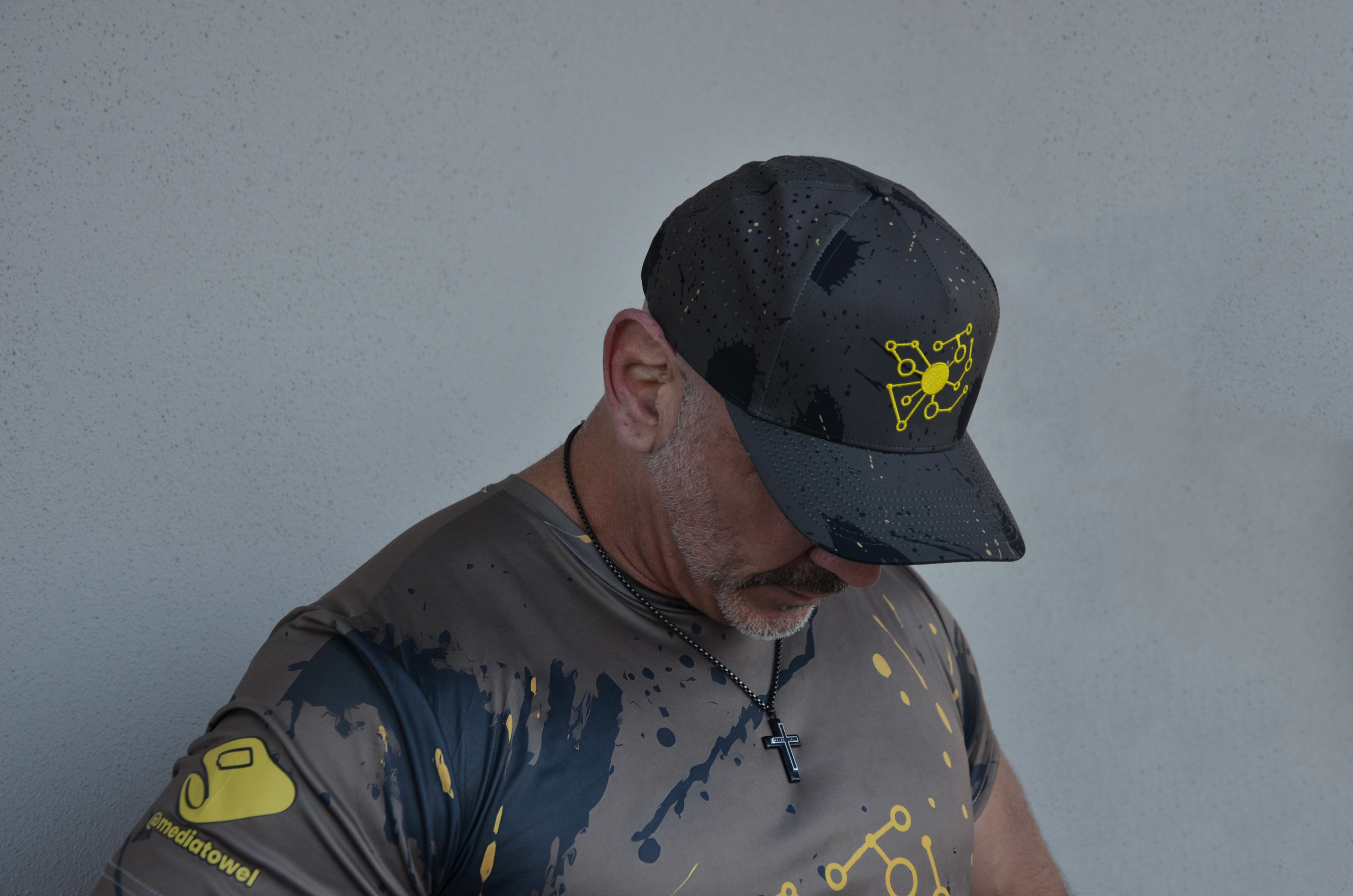 Man wearing a dark camo cap with a yellow logo and a matching shirt.