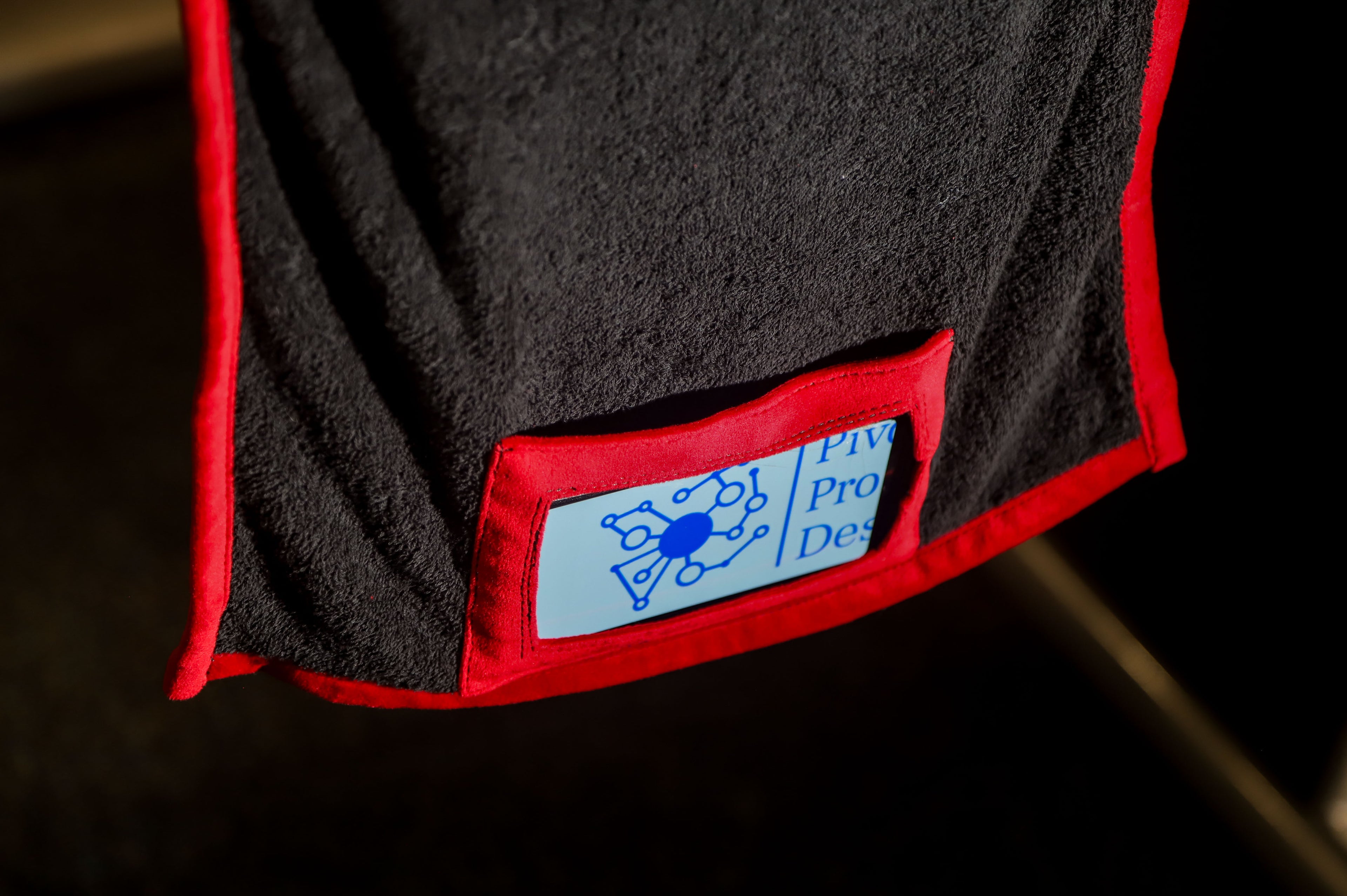 Black towel with red border and a blue label on a dark background