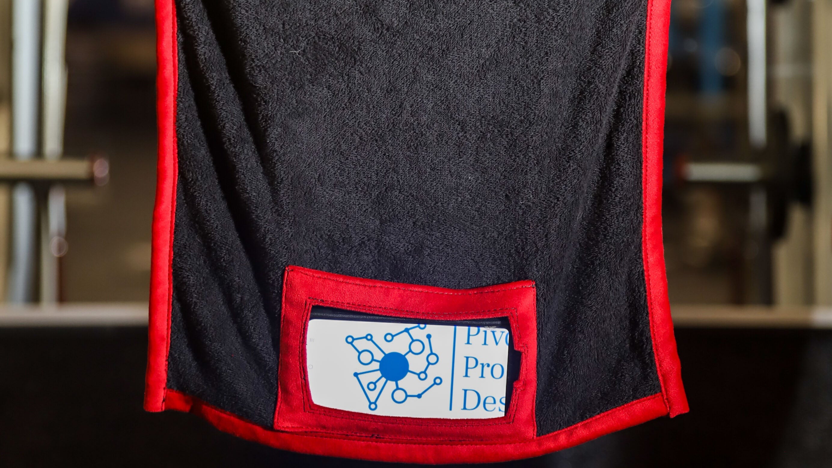 Black towel with red trim hanging on a rack in a gym setting