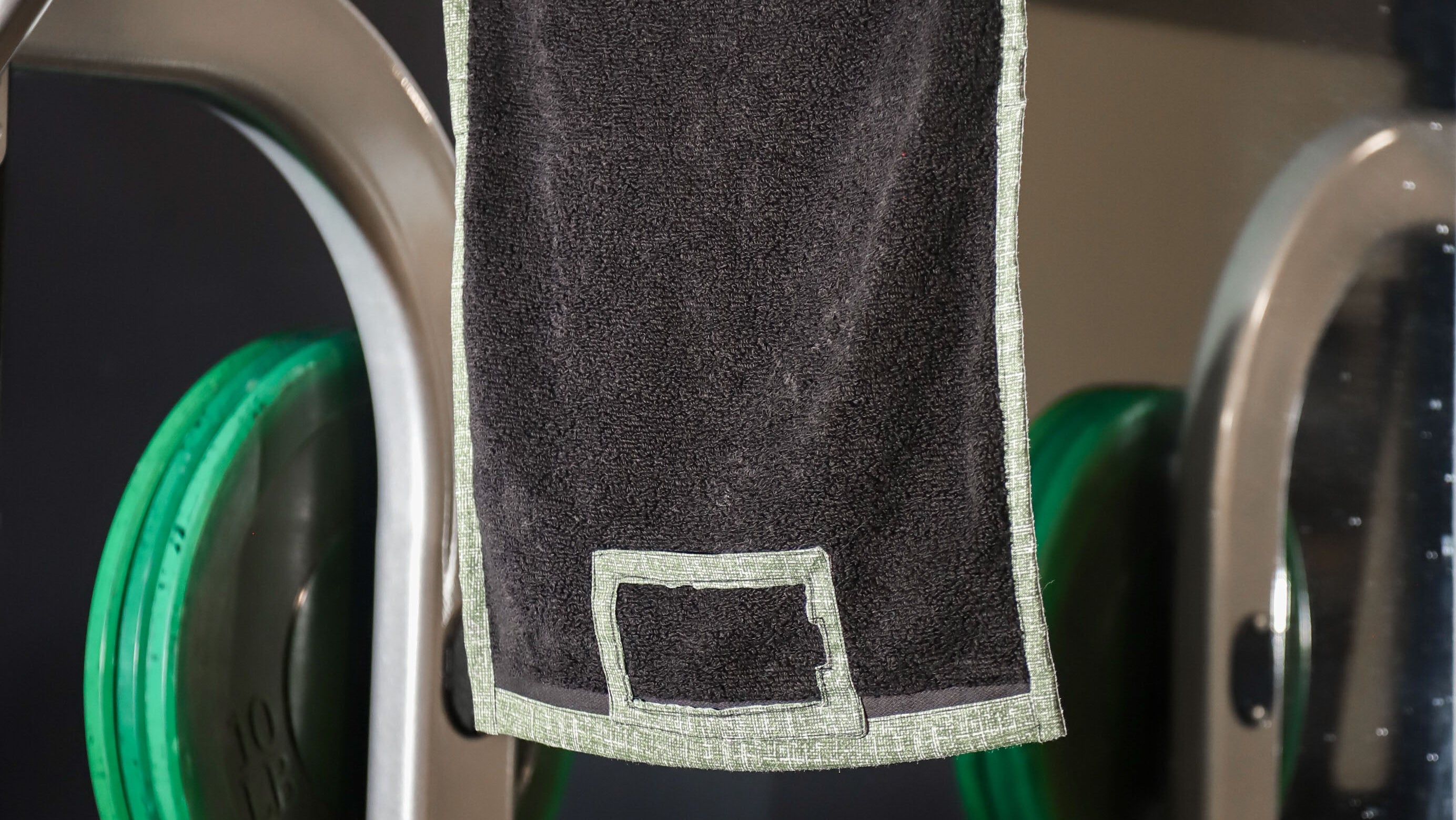 Black towel hanging on a rack with gym equipment in the background