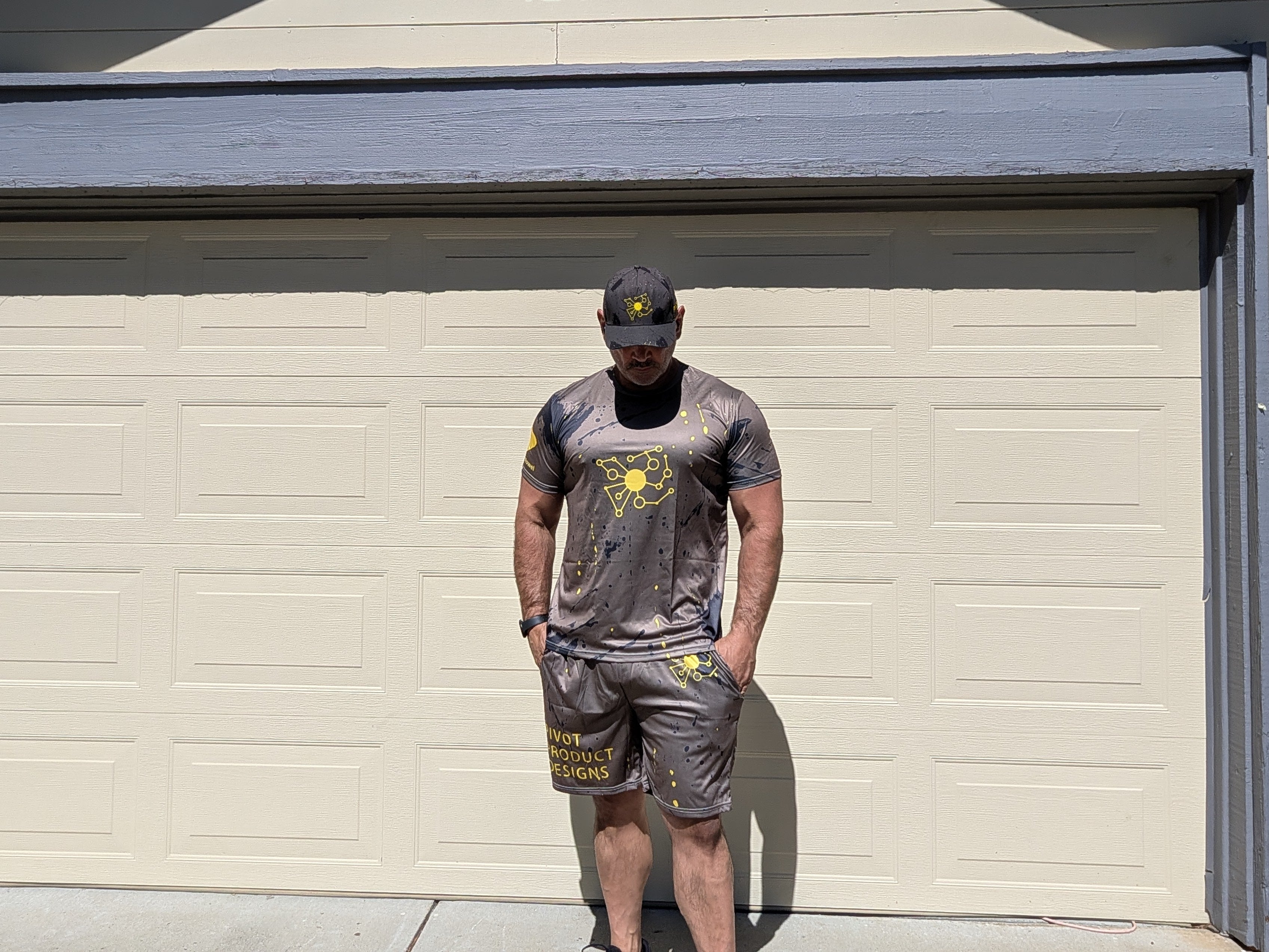 Big Mike wearing the full Pivot Performance Set Bundle — Tee, Shorts, and Hat together, charcoal black with yellow splatter print