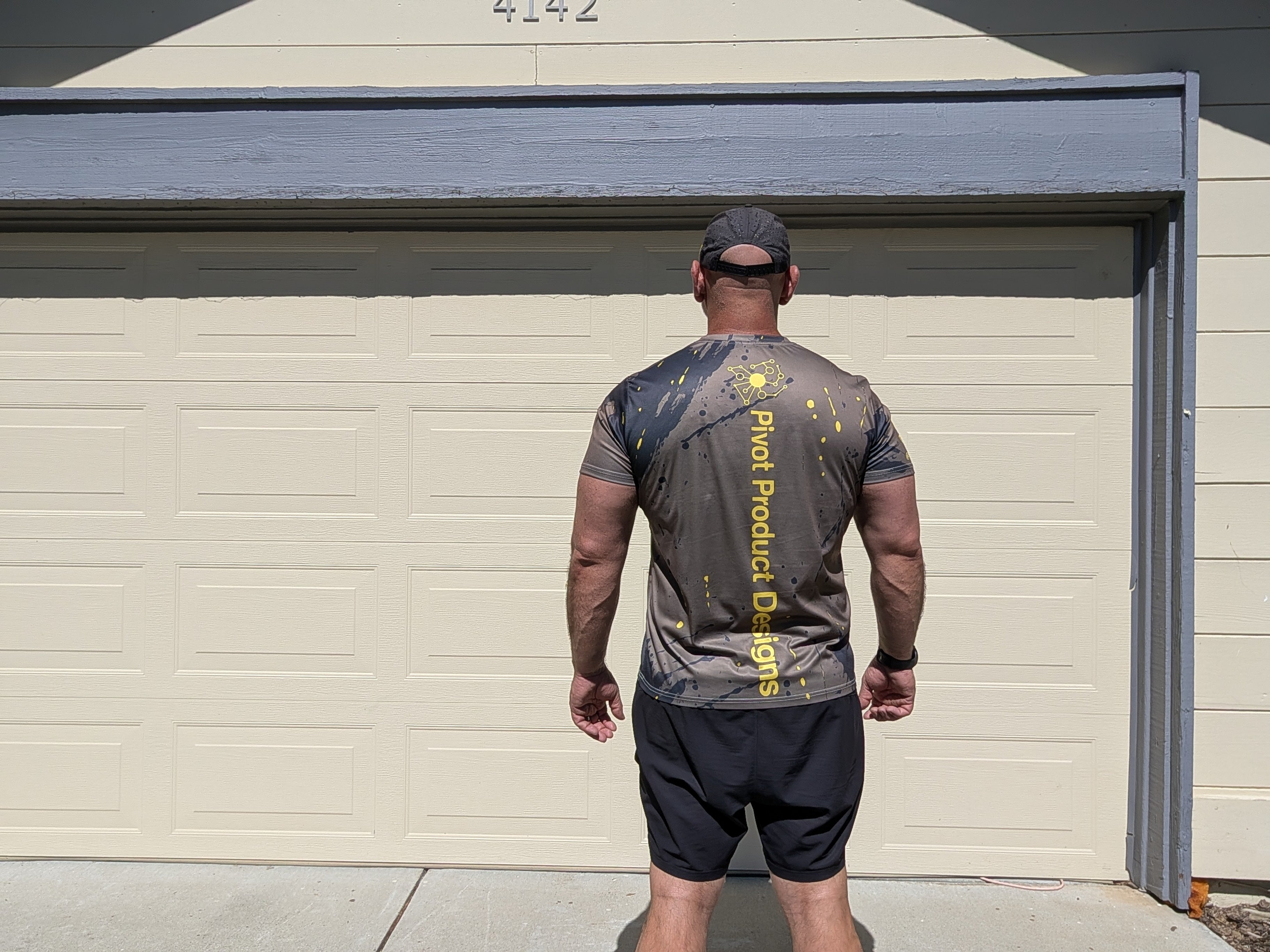 Back view of the Pivot Performance Tee showing the PIVOT PRODUCT DESIGNS wordmark and yellow splatter print on charcoal black fabric