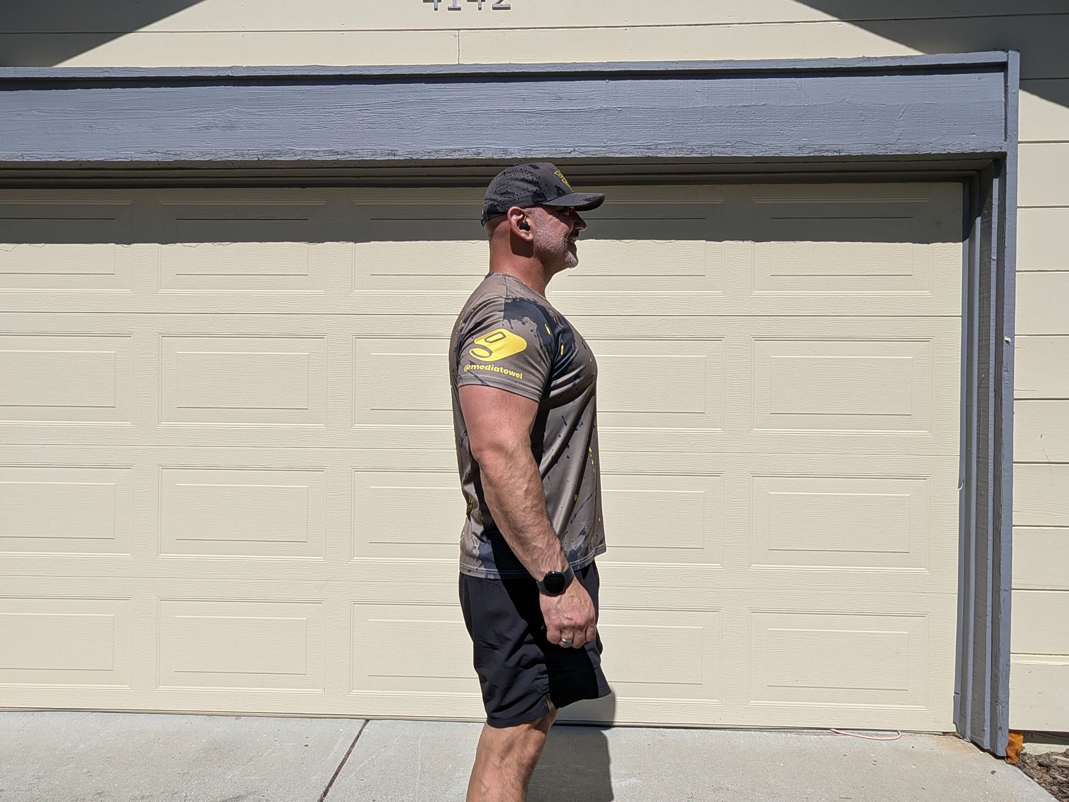 Side profile of the Pivot Performance Tee on Big Mike — charcoal black athletic fit performance fabric with yellow splatter print