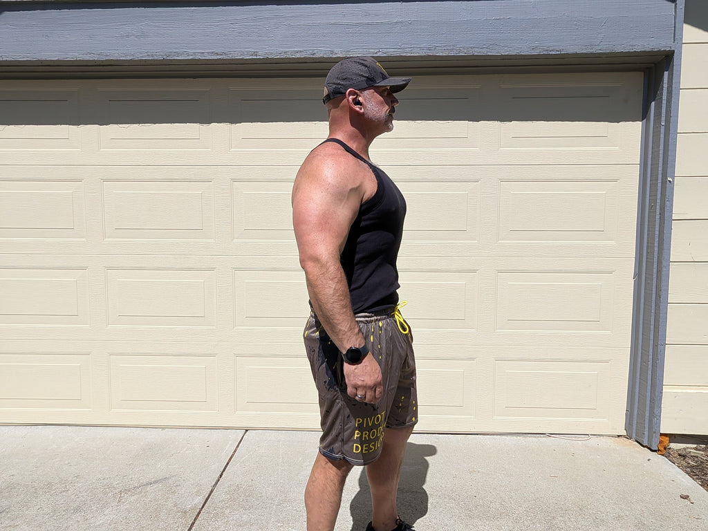 Side view of the Pivot Performance Shorts on Big Mike — yellow PIVOT PRODUCT DESIGNS leg wordmark visible on charcoal fabric